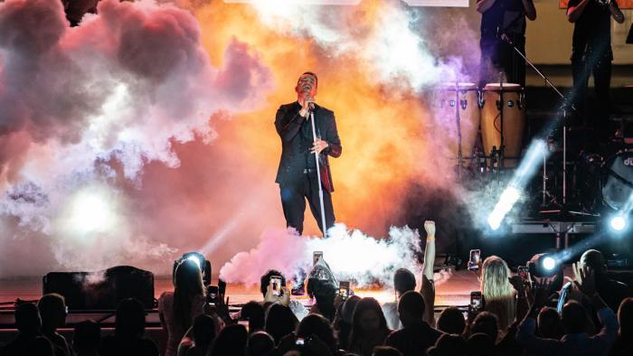 A performer stands on stage accented by smoke and a light show